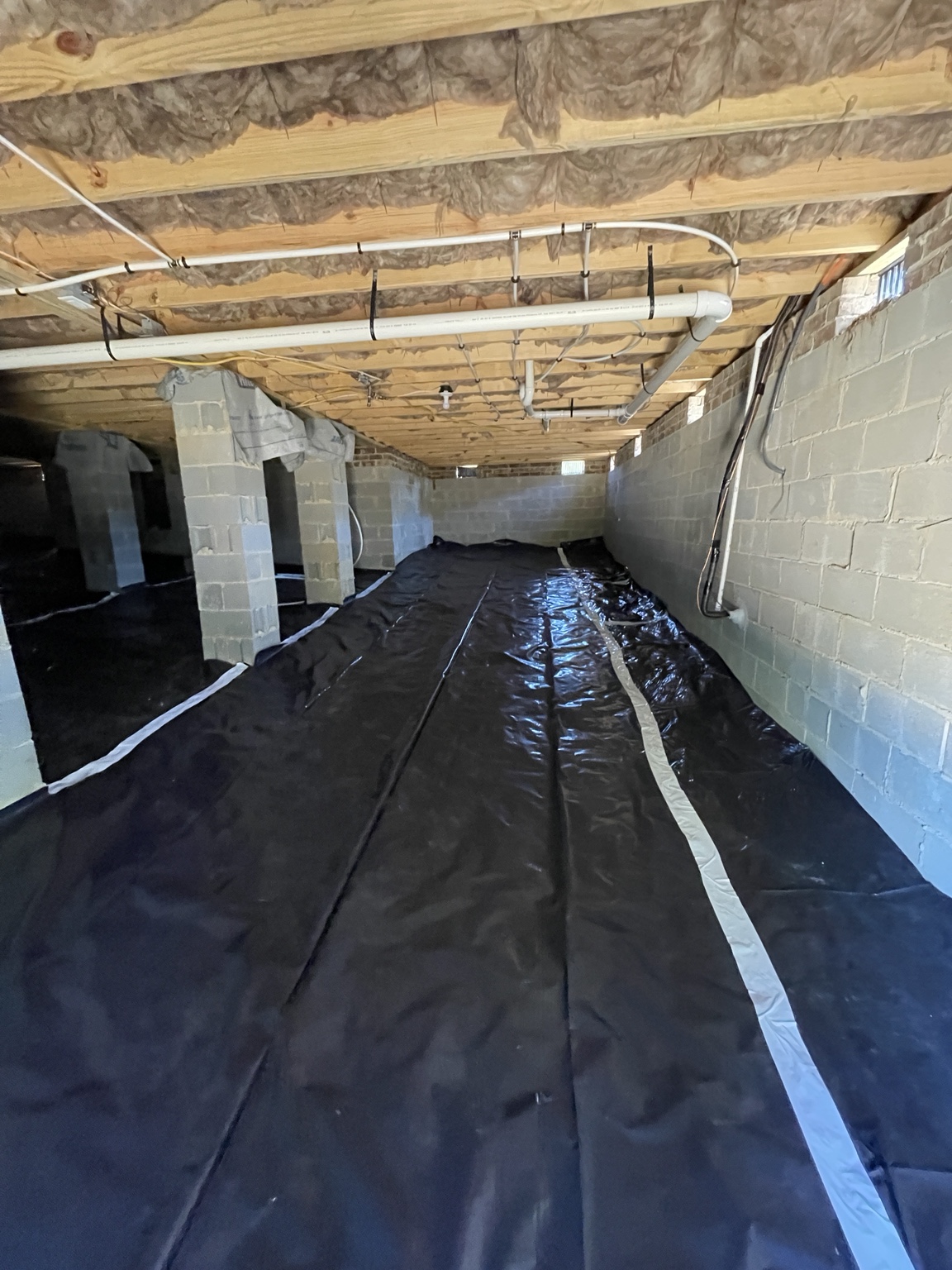 Black crawlspace vapor barrier installed across the ground and sealed at supports